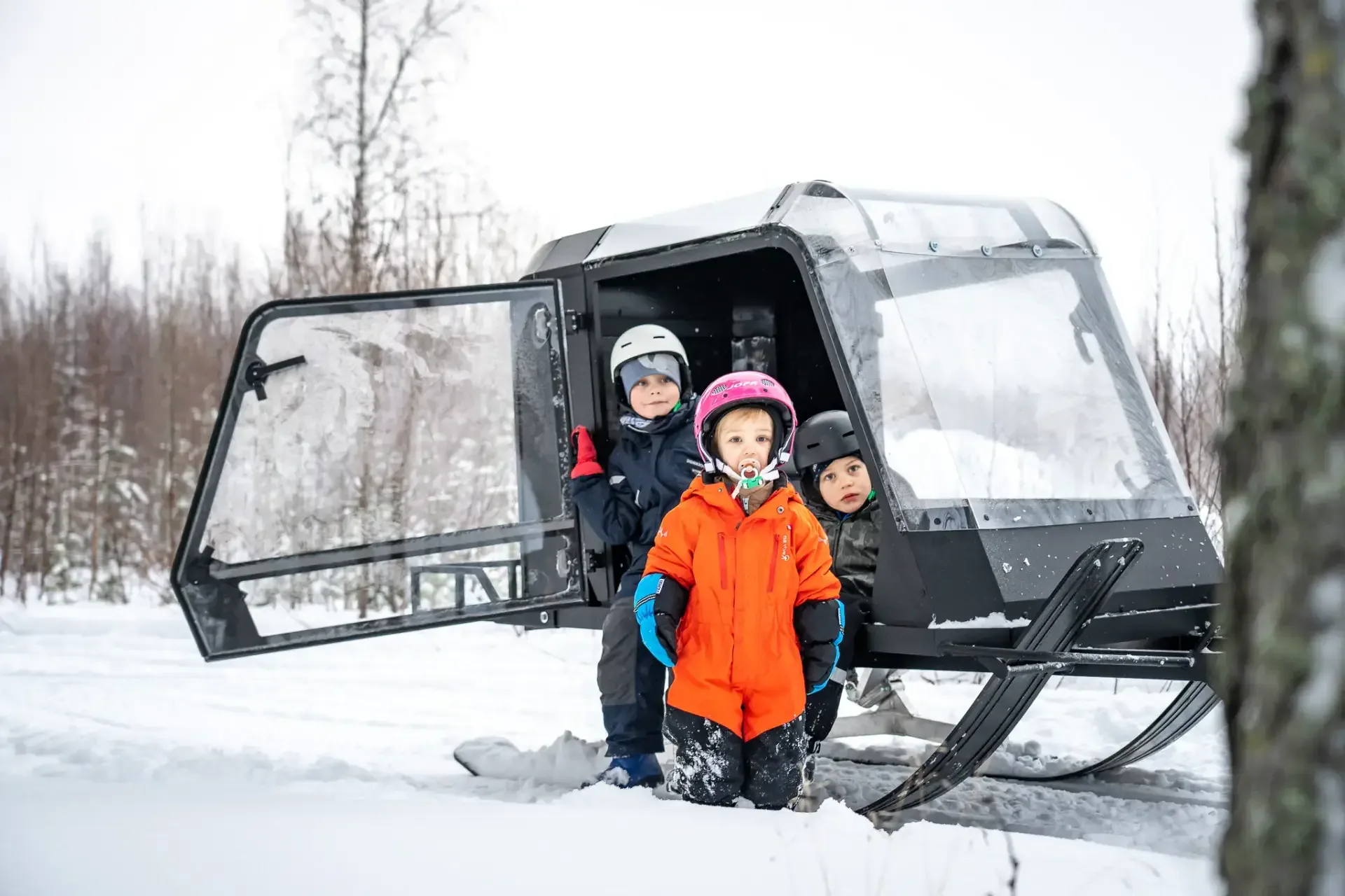 Tre barn i vinterkläder står vid den öppna dörren på Pulkapanorama Expedition