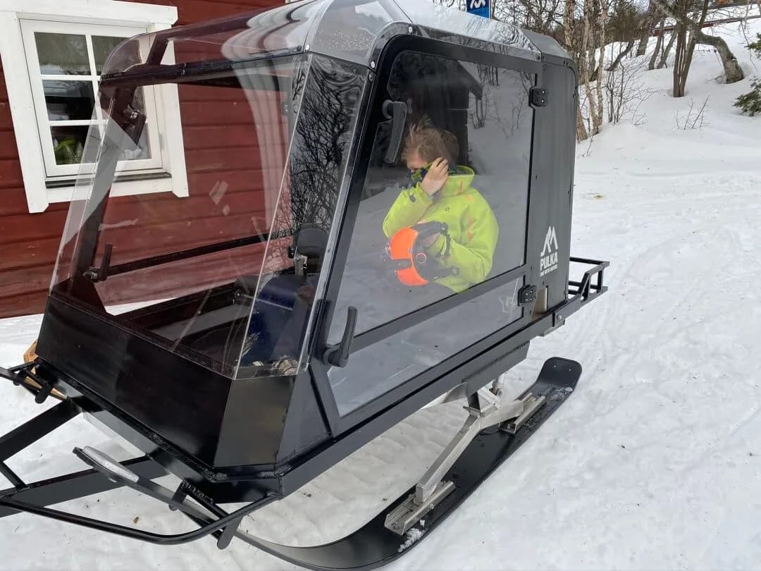Barn i Pulkapanorama utanför en röd stuga