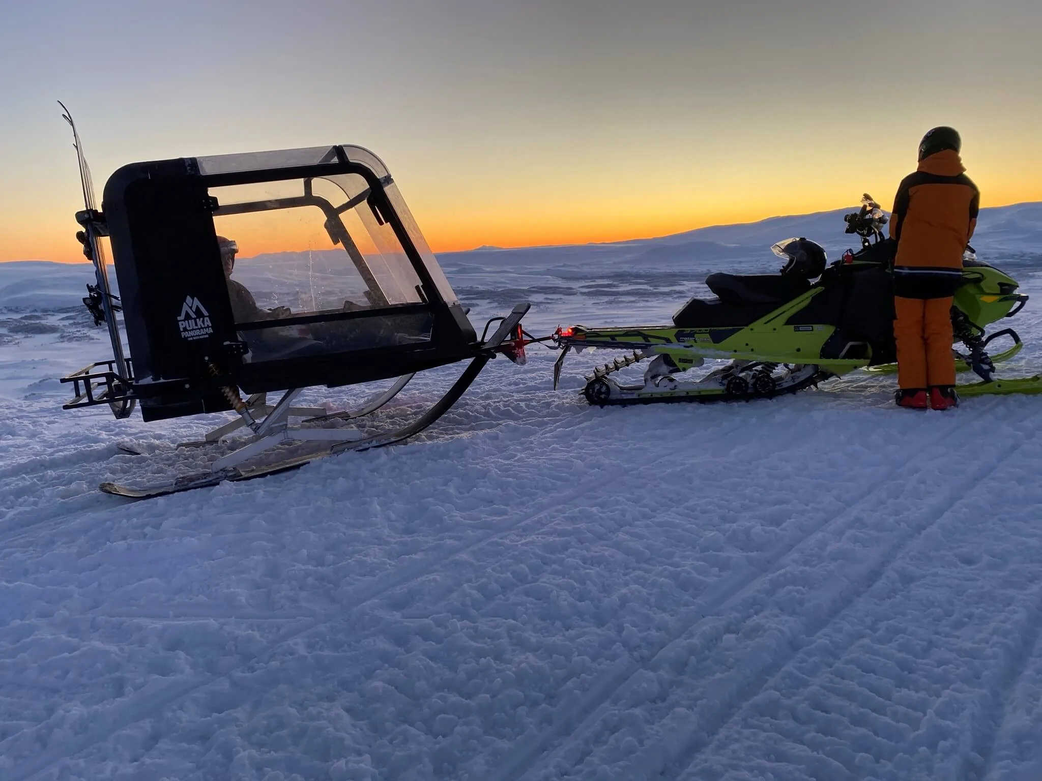 Familj vid Pulkapanorama och snöskoter på fjället i skymningen